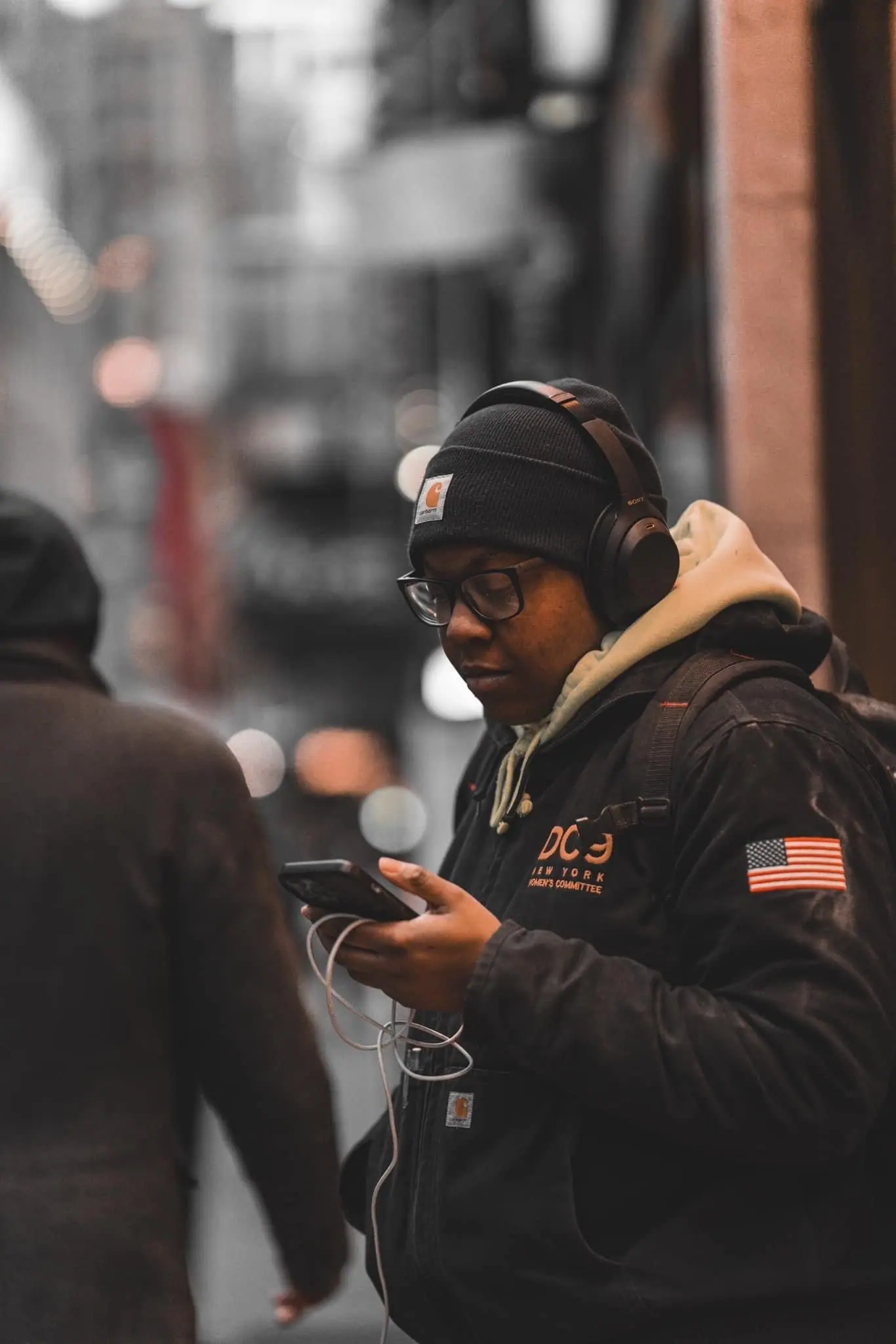 Urban street scene with person wearing black jacket and American flag patch.